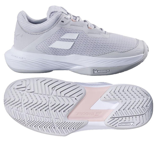 The Babolat SFX 4 All Court 2025 Women's Tennis Shoes in Lunar Rock combine comfort and style with a white design featuring light gray mesh and solid overlays. They offer a prominent tread pattern, with visible branding on the side and sole. The image displays both side and sole views.