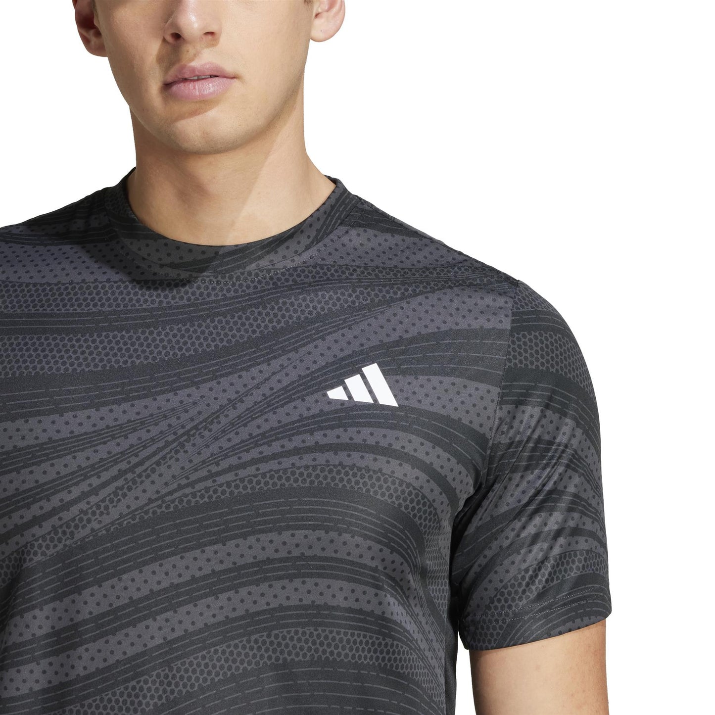 A person models the ADIDAS Mens Club Graphic Tennis T-Shirt - Black, featuring a white logo on the chest against its dark, patterned design. Made from recycled materials and utilizing AEROREADY technology for comfort, it stands out against a plain white background showcasing only the upper body.