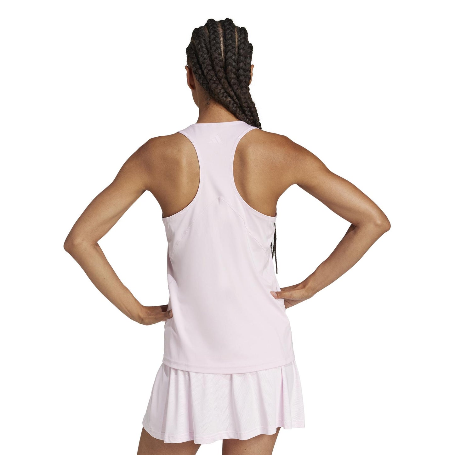 A person with braided hair, back turned, wears the light pink ADIDAS Women's Club Tennis Tank Top by adidas, showcasing its racerback style made from recycled materials with hands on hips.