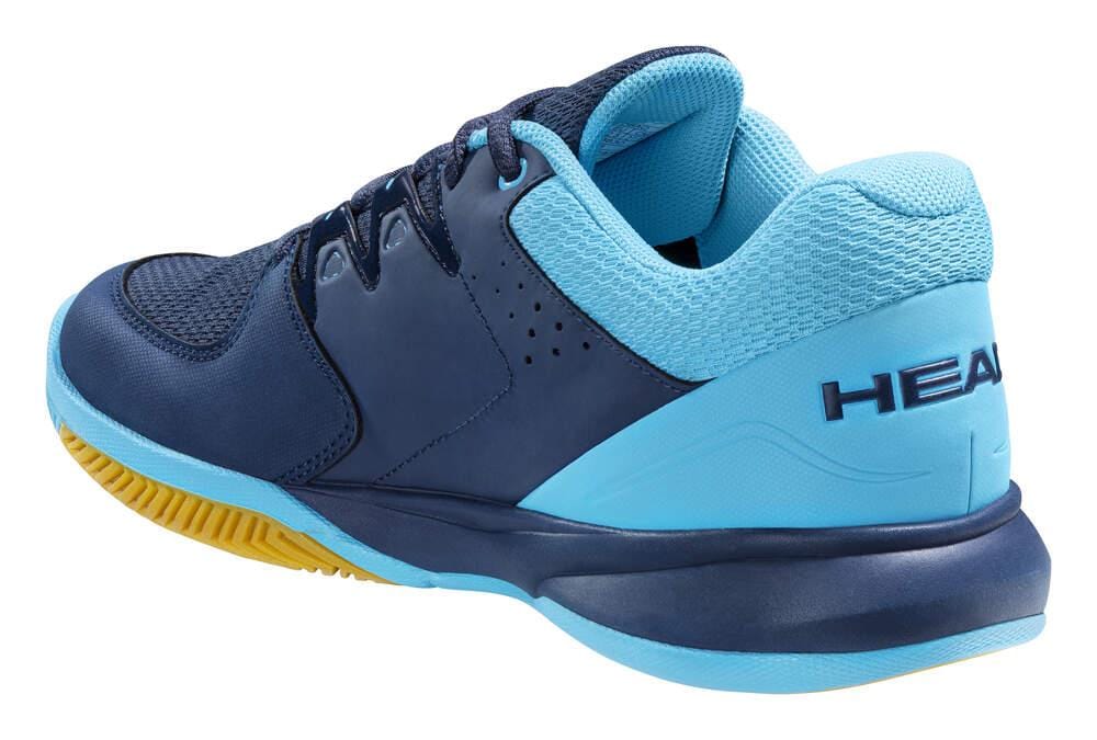 A detailed view of the HEAD Grid 3.5 Indoor Court Tennis Shoes in dark blue and aqua showcases its textured yellow sole and prominently displays the brand name "HEAD" on the heel. This shoe includes a lace-up fastening system, a cushioned collar for added comfort, an EVA midsole, and breathable mesh to improve airflow.