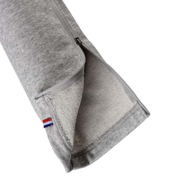 A close-up of silver fabric from the Tecnifibre Unisex Team Tennis Pants, with a zipper partially open to reveal the inner lining. A small tag featuring red, white, and blue stripes is visible on the seam near the zipper.