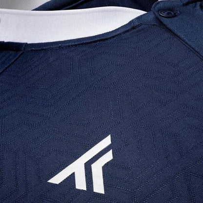 Close-up of a Tecnifibre Mesh Polo Shirt in the Marine color, showcasing its breathable polyester mesh fabric with a subtle geometric pattern. The chest area features a white logo resembling stylized letters or arrows, complemented by a crisp white neckline and buttons at the top.