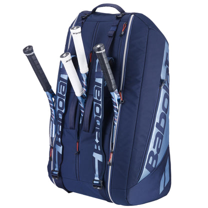 The Babolat RH12 Pure Drive Gen11 12 Racket Tennis Bag in navy blue is shown upright, holding three rackets with white grips peeking from its large compartments. This bag features multiple zippers and a convenient carrying strap.