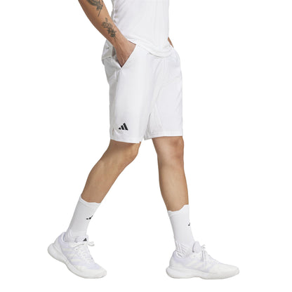 In an all-white ensemble, a person wears Adidas Men's 3 Stripe Tennis Shorts in White. They're mid-stride, revealing arm tattoos against a seamless white backdrop.