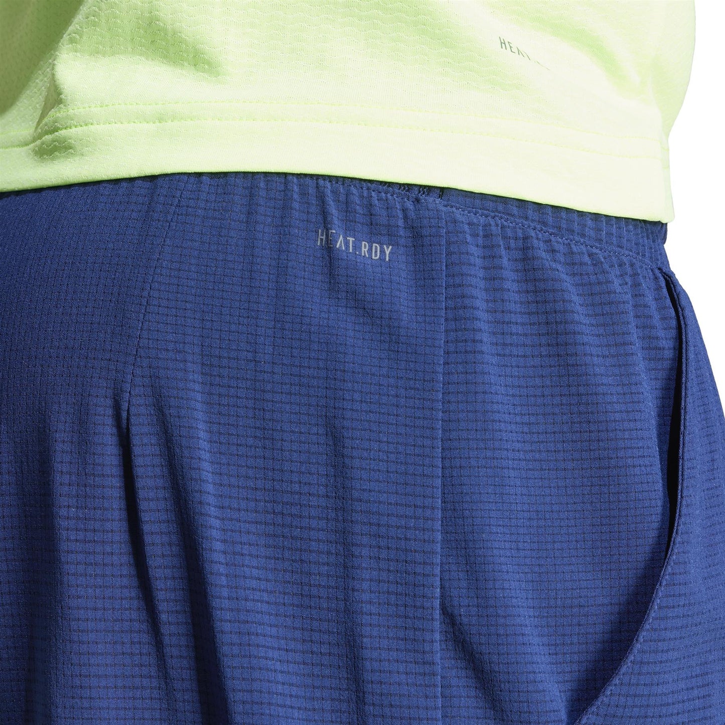 Close-up of a person wearing a light green top and navy ADIDAS Ergo Mens Tennis Shorts. The lightweight, breathable fabric is made from recycled materials, featuring "HEAT.RDY" for optimal temperature control and comfort.