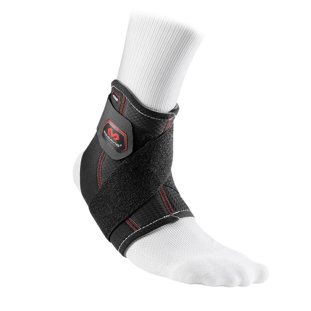 A foot in a white sock is wrapped in the McDavid Ankle Support With Strap (432R), featuring black fabric with red stitching and a side logo. Designed for injury prevention, it offers adjustable straps for optimal support and compression.