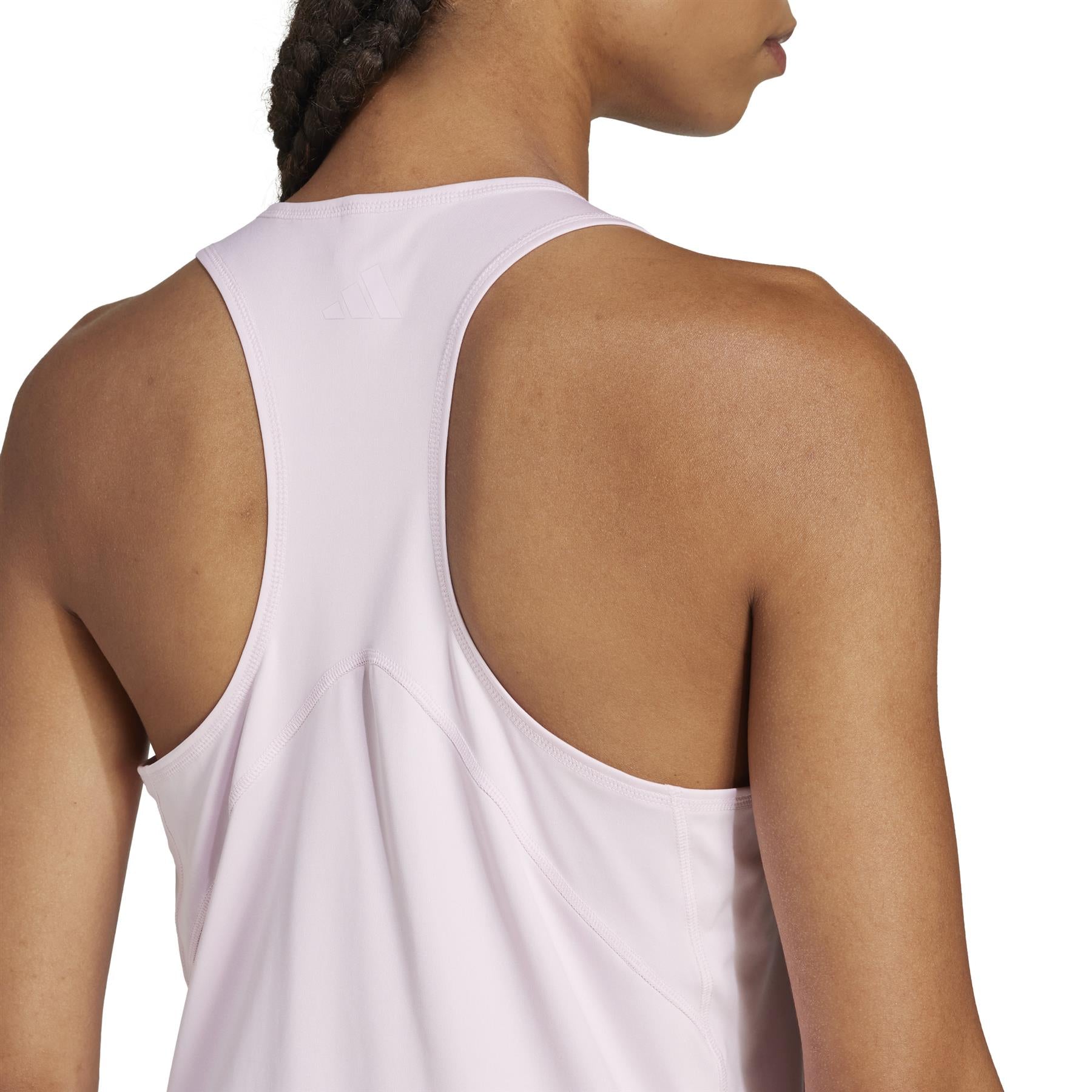 A person stands sideways wearing the ADIDAS Women's Club Tennis Tank Top in light pink by adidas. This sleeveless, racerback top is made from recycled materials and features CLIMACOOL technology, accentuating their upper body and braided hair.