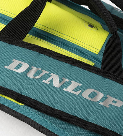 Close-up of a Dunlop SX Performance 12 Racket Tennis Bag, showcasing a teal, black, and yellow design. "Dunlop" stands out in bold silver on the teal area. Ergonomic shoulder straps are shown crossing over the yellow zipper.