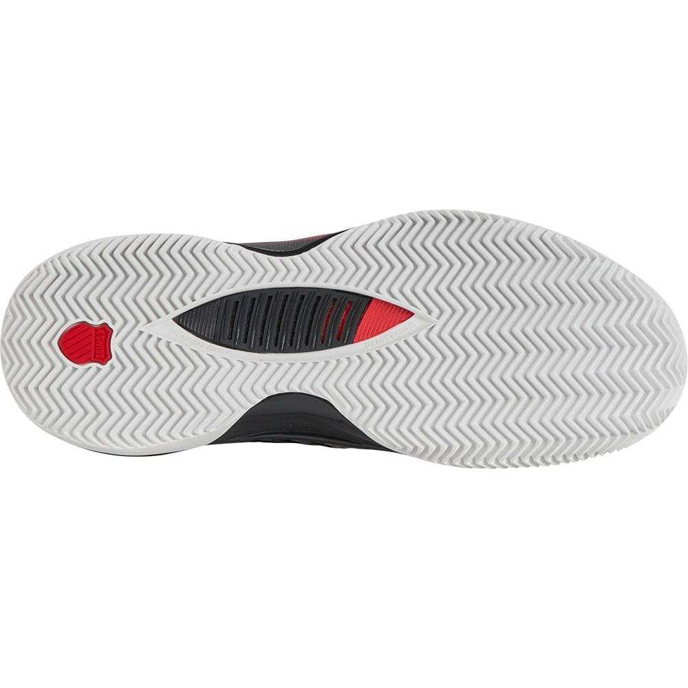 The image highlights the sole of a K-Swiss Hypercourt Supreme 2 men's tennis shoe in Bright White / Stretch Limo / High Risk Red, featuring white zigzag tread patterns. A red hexagonal section near the heel and a black ventilation area in the center improve grip and flexibility. The cutting-edge Durawrap X design ensures durability on the court.