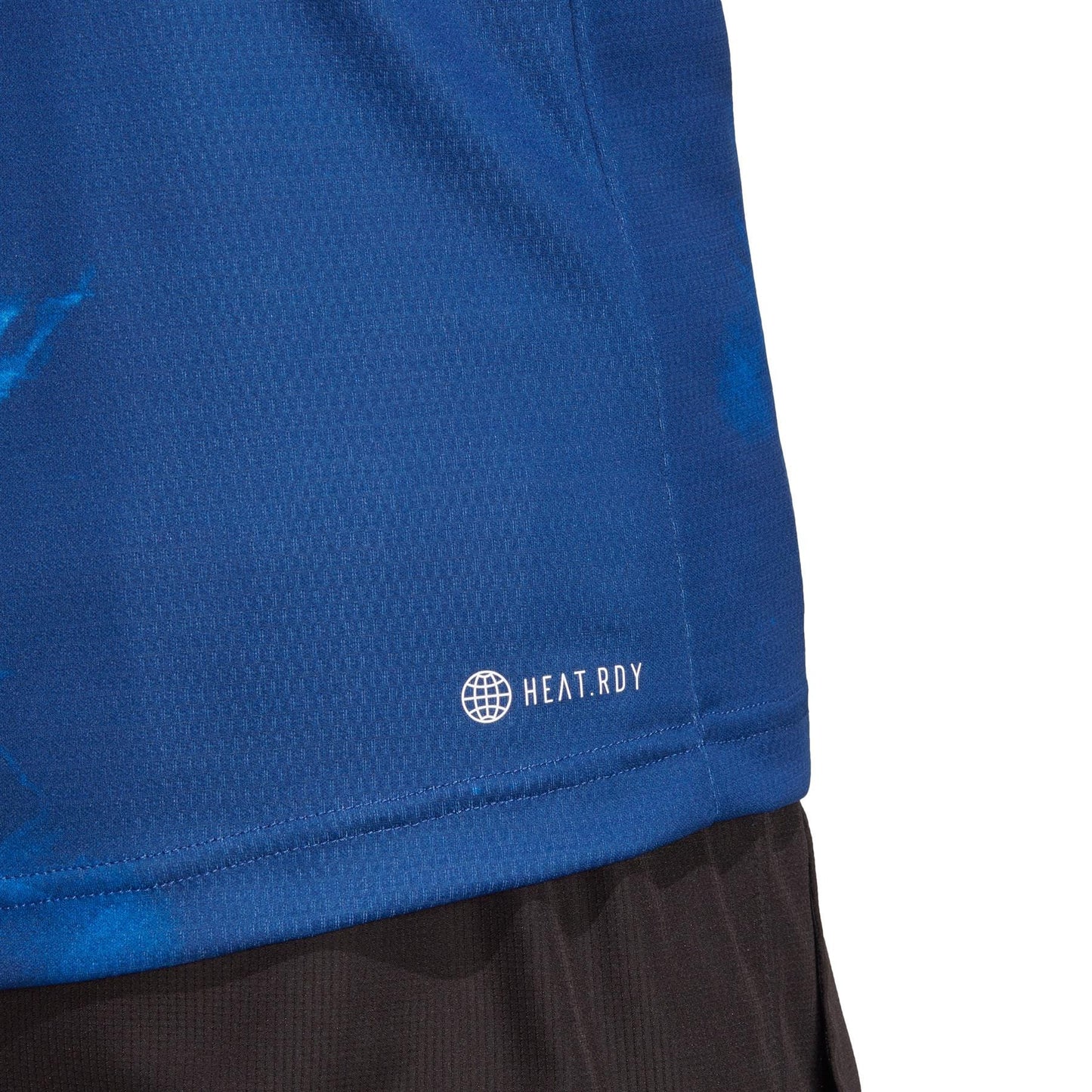 Close-up of a person wearing the blue adidas Melbourne Mens Freelift Tennis Polo Shirt, with "HEAT.RDY" text near the hem. The shirt features a textured pattern that helps players stay cool during the Australian Open, paired with black shorts.